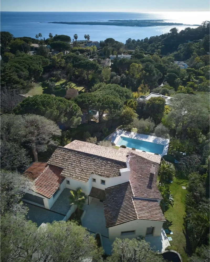 Vue aérienne d’une villa aux toits de tuiles, avec piscine, dans les pins face à la mer.